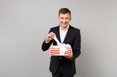 Genç gülümseyen iş adamı açılış kırmızı elbiseli gri arka plan üzerinde izole hediye kurdele ile mevcut kutusu çizgili. Başarı kariyer servet iş. Sevgililer, kadınlar günü Doğum günü, tatil kavramı