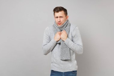 Gri süveterli genç adam buz gibi göğsüne elele eşarp ayakta gri duvar arka plan üzerinde izole. Sağlıklı moda yaşam tarzı, insanlar samimi duygular, soğuk sezon kavramı. Kopyalama alanı alay