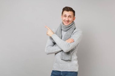 Yakışıklı genç gri süveterli işaret parmağı bir kenara gri duvar arka plan üzerinde izole eşarp. Sağlıklı moda, yaşam tarzı insanların samimi duygular, soğuk sezon kavramı. Kopyalama alanı alay