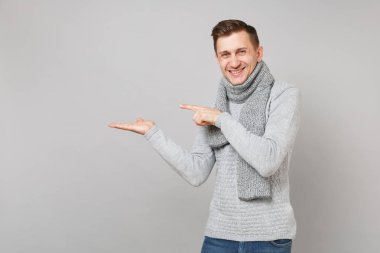 Gri kazak, eşarp işaret parmağı, bir kenara gri duvar arka plan üzerinde izole el gülümseyen genç adam. Sağlıklı moda yaşam tarzı insanların samimi duygular, soğuk sezon kavramı. Kopyalama alanı alay