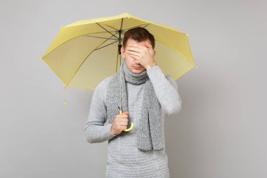 Genç adam gri süveterli eşarp gri arka plan üzerinde izole el ile yüz kapsayan sarı şemsiye tutan. Sağlıklı moda yaşam tarzı insanların samimi duygular soğuk sezon kavramı. Kopyalama alanı alay