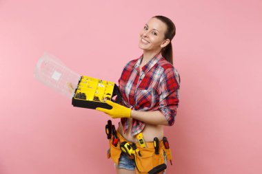 Ekose gömlek, kot şort, kadında güçlü genç tamirci Seti Araçları farklı enstrümanlar, pembe arka plan izole araç kutusu tutarak dolu kemer. Kadın erkek iş. Yenileme işgal kavramı