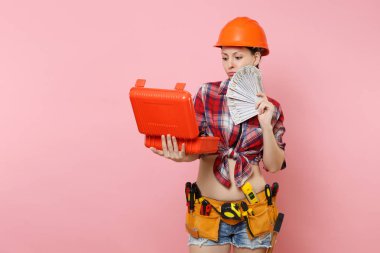 Güçlü kadın portakal kask, ekose gömlek, kot şort seti araçları tam aletleri, araç kutusu, çok nakit para, pembe arka plan izole bant. Kadın erkek iş. Yenileme işgal kavramı
