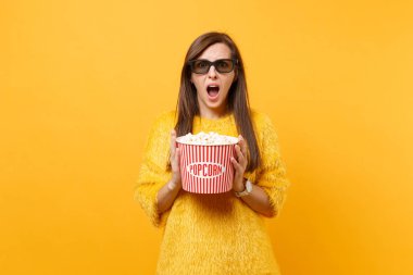 Portresi korktuğunu kova patlamış mısır tutan genç kız kürk kazaklı, 3d IMAX gözlük film filmi izlerken parlak sarı arka plan üzerinde izole şok. İnsanlar sinema, samimi duygular yaşam tarzı
