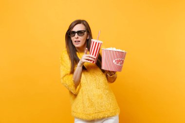 Genç kadın parmağı işaret, kova patlamış mısır bardak kola veya izole sarı zemin üzerine soda tutun film film izlerken 3d IMAX bardaklarda korkuttu. İnsanlar sinema, samimi duygular yaşam tarzı