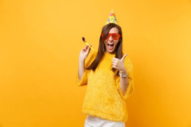 Neşeli kadın portakal komik gözlük, başparmak yukarı, parlak sarı arka plan üzerinde izole kutlama gösterilen boru oynama ile Doğum günü şapkası. İnsanlar samimi duygular yaşam tarzı kavramı. Reklam alanı