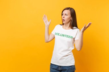 İzole sarı arka plan üzerinde beyaz t-shirt ile yazılı yazıt yeşil başlık gönüllü korkmuş şok korkmuş genç kadın portresi. Gönüllü ücretsiz destek yardım, sadaka grace iş kavramı