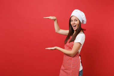 Ev hanımı kadın şef aşçı ya da baker izole kırmızı duvar arka plan üzerinde çizgili önlük, beyaz tişört, toque şefler şapkalı. Mutlu kahya kadın gösteren boyutu el hareketi. Kopyalama alanı kavramı alay