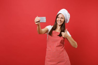 Ev hanımı kadın şef aşçı ya da baker izole kırmızı duvar arka plan üzerinde çizgili önlük, beyaz tişört, toque şefler şapkalı. Eğlence gülümseyen kadın selfie cep telefonu üzerinde atış yapıyor. Kopyalama alanı kavramı alay