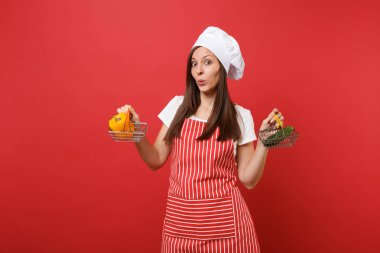 Ev hanımı kadın şef aşçı baker şapkalı izole kırmızı duvar arka plan üzerinde çizgili önlük beyaz t-shirt toque şefler. Kadın tutun sarı biber salatalık bakkal itme arabası sahte kopya alanı kavramı kadar
