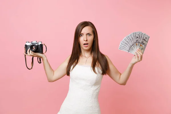 困惑した花嫁ウェディング ドレス保持しているレトロなビンテージ写真カメラ 女性は 現金お金選択するスタッフ ピンクの背景に分離された写真家の多くをバンドルします 結婚式のリストを行う組織 — ストック写真