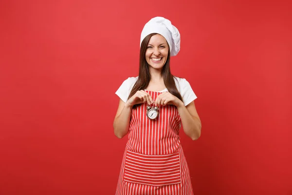 Housewife female chef cook or baker in striped apron, white t-shirt, toque chefs hat isolated on red wall background. Smiling woman hold in hand retro alarm clock hurry up. Mock up copy space concept