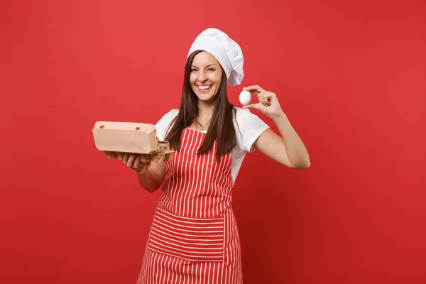Housewife female chef cook or baker in striped apron t-shirt toque chefs hat isolated on red wall background. Woman hold brown craft cardboard container for chicken eggs. Mock up copy space concept