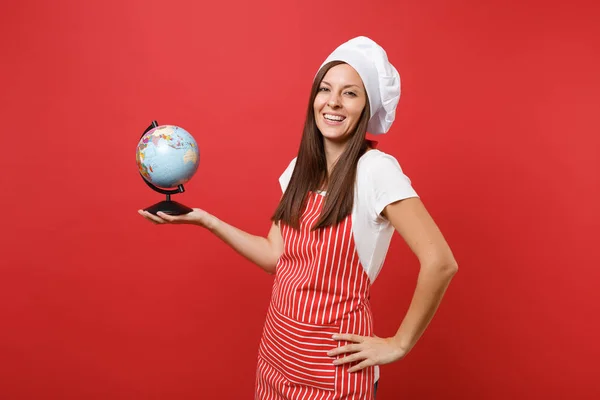 Housewife female chef cook or baker in striped apron, white t-shirt, toque chefs hat isolated on red wall background. Housekeeper woman holding in palms Earth world globe. Mock up copy space concept