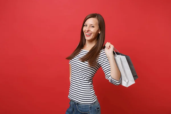 赤い壁の背景に分離されたショッピング後購入パッケージ袋を保持しているストライプの服で笑顔の若い女性の肖像画 の心から感情 ライフ スタイルのコンセプト コピー スペースをモックアップします — ストック写真