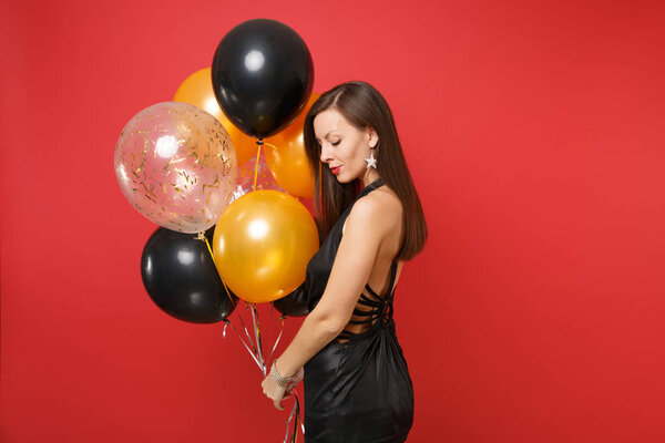 Elegant young girl in little black dress celebrating holding air balloons isolated on red background. St. Valentine's, International Women's Day, Happy New Year, birthday mockup holiday party concept