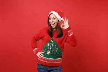 Ağız açık tutmak Noel şapkalı heyecanlı Noel Baba kız, seyir Ok hareket izole kırmızı arka plan üzerinde gösterilen şaşırttı. Mutlu yeni yıl 2019 kutlama tatil parti kavramı. Kopyalama alanı alay