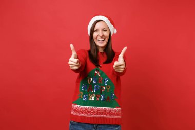 Mutlu neşeli Noel Baba içindeki genç kız örgü kazak, başparmak gösterilmesini Noel şapka parlak kırmızı duvar arka plan üzerinde izole. Mutlu yeni yıl 2019 kutlama tatil parti kavramı. Kopyalama alanı alay