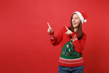 Komik Noel Baba kız örme kazak, Noel şapka Dizin bir kenara parlak kırmızı duvar arka plan üzerinde izole parmakları işaret içinde. Mutlu yeni yıl 2019 kutlama tatil parti kavramı. Kopyalama alanı alay