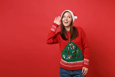 Meraklı genç Noel Baba kız örgü kazak, Noel şapka kulak misafiri, parlak kırmızı duvar arka plan üzerinde izole işitme jest. Mutlu yeni yıl 2019 kutlama tatil parti kavramı. Kopyalama alanı alay