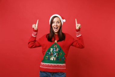 Genç Santa geniş açık ve işaret işaret parmakları ağız uydurarak Noel şapkalı kız kırmızı zemin üzerine izole şaşırttı. Mutlu yeni yıl 2019 kutlama tatil parti kavramı. Kopyalama alanı alay
