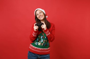 Rüya gibi genç Noel Baba kız kazak Noel şapka kırmızı duvar arka plan üzerinde izole joystick ile bilgisayar oyunu oynamak arıyorsunuz. Mutlu yeni yıl 2019 kutlama tatil parti kavramı. Kopyalama alanı alay