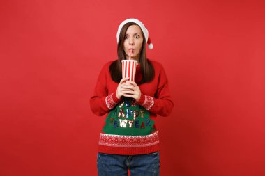 Noel Baba kız örgü kazak, Noel şapka içme cola veya soda plastik fincan izole kırmızı zemin üzerine şok. Mutlu yeni yıl 2019 kutlama tatil parti kavramı. Kopyalama alanı alay