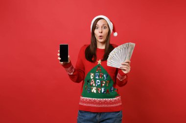 Kırmızı zemin üzerine izole boş boş ekran ile çok avuç dolar banknotlar, nakit para ve cep telefonu tutan genç Noel Baba kız hayran. Mutlu yeni yıl 2019 kutlama tatil parti konsept