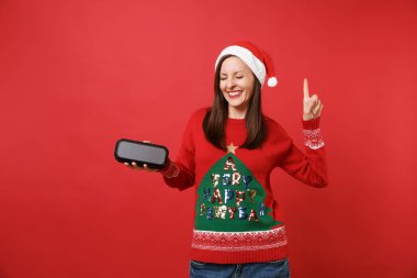 Gülümseyen genç Noel Baba kız ile işaret parmağı yukarıyı, taşınabilir kablosuz bluetooth müzik hoparlör izole kırmızı zemin üzerine tutarak gözler kapalı. Mutlu yeni yıl 2019 kutlama tatil parti konsept