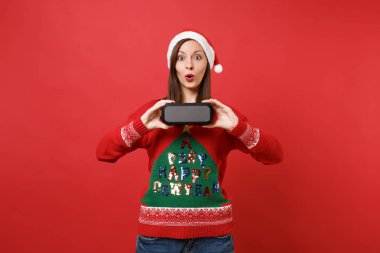 Sürpriz, ağzı geniş açık tutarak genç Noel Baba kız holding taşınabilir kablosuz bluetooth müzik hoparlör izole kırmızı zemin üzerine hayran. Mutlu yeni yıl 2019 kutlama tatil parti konsept