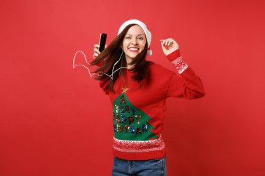 Noel Baba kız cep telefonu, müzik dinleme tutan studio, atlama kulaklık ile gülümseyen izole kırmızı zemin üzerine. Mutlu yeni yıl 2019 kutlama tatil parti kavramı. Kopyalama alanı alay