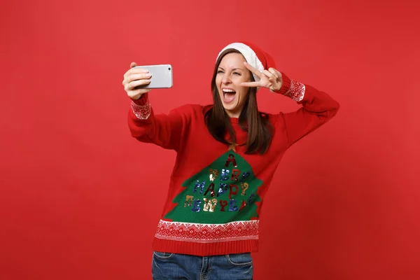開いた口を取る Selfie をやって面白いサンタ少女は 赤い背景に分離された勝利のサインを示す携帯電話で撮影 幸せな新しい年 2019年お祝いの休日党の概念 コピー スペースをモックアップします — ストック写真