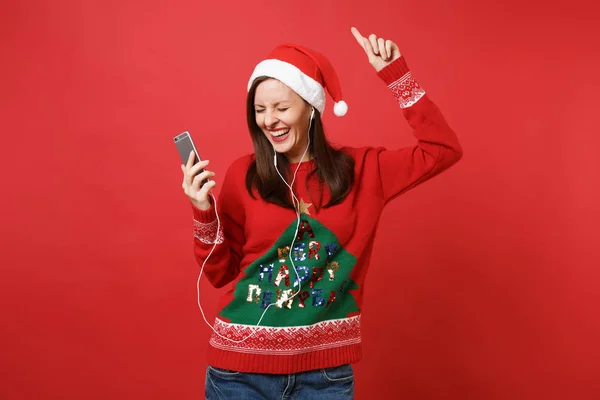 陽気なサンタ少女保持携帯電話 音楽を聴いて イヤホンでの手の上昇はダンス赤の背景に分離されました 幸せな新しい年 2019年お祝いの休日党の概念 コピー スペースをモックアップします — ストック写真
