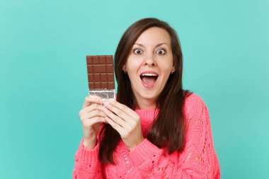 Örgü pembe kazaklı ağız tutmak heyecanlı genç kadın aç, sürpriz arıyor tutun el çikolata mavi arka plan, stüdyo portre izole. İnsanlar yaşam tarzı kavramı. Kopyalama alanı alay