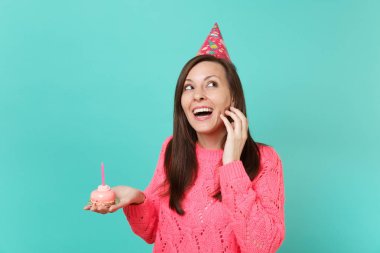 Örgü pembe kazaklı, bakılması, Doğum günü şapka neşeli genç kadın elinde tutan pasta mum ile mavi duvar arka plan stüdyo portre üzerinde izole. İnsanlar yaşam tarzı kavramı. Kopyalama alanı alay