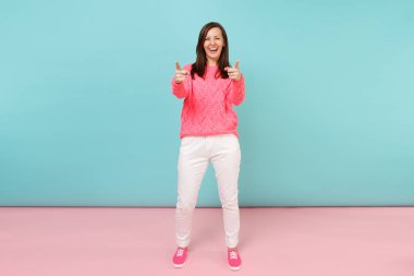 Tam uzunlukta örme gül kazaklı gülümseyen genç kadın portresi, beyaz parlak pembe mavi pastel duvar arka planda Studio izole poz pantolon. Moda yaşam tarzı kavramı. Kopyalama alanı alay