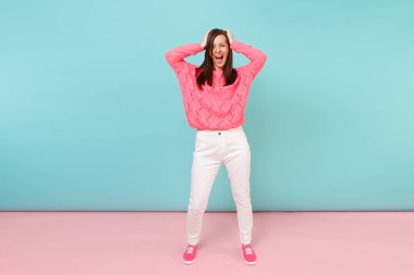 Tam uzunlukta örme gül kazaklı gülümseyen genç kadın portresi, beyaz parlak pembe mavi pastel duvar arka planda Studio izole poz pantolon. Moda yaşam tarzı kavramı. Kopyalama alanı alay