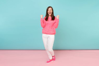 Tam uzunlukta örme gül kazaklı gülümseyen genç kadın portresi, beyaz parlak pembe mavi pastel duvar arka planda Studio izole poz pantolon. Moda yaşam tarzı kavramı. Kopyalama alanı alay