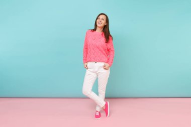 Tam uzunlukta örme gül kazaklı gülümseyen genç kadın portresi, beyaz parlak pembe mavi pastel duvar arka planda Studio izole poz pantolon. Moda yaşam tarzı kavramı. Kopyalama alanı alay