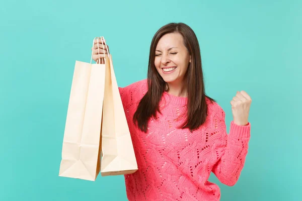 快乐的年轻女子在针织粉红色毛衣做优胜者姿态 拿着包裹袋子与购买以后购物查出在蓝色墙壁背景 人的生活方式概念 模拟复制空间 — 图库照片
