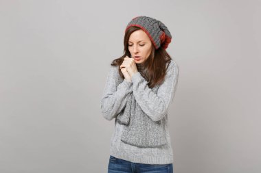 Genç kadın gri kazak, şapka ve atkı indirdi kafa elleri ısınma ile gri arka plan üzerinde izole. Sağlıklı moda yaşam tarzı, insanlar samimi duygular, soğuk sezon kavramı. Kopyalama alanı alay
