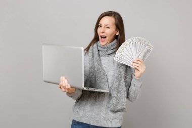 Yanıp sönen kadın kazaklı dizüstü pc bilgisayar, gri arka plan üzerinde izole dolar banknotlar nakit para tutun birçok grup üzerinde çalışıyor. Sağlıklı yaşam online tedavi soğuk sezon kavramı danışmanlık