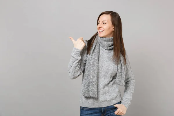 年轻女子穿着灰色毛衣 围巾指着拇指一边孤立在灰色的墙壁背景 工作室的肖像 健康时尚的生活方式 人真诚的情感 寒冷的季节理念 模拟复制空间 — 图库照片
