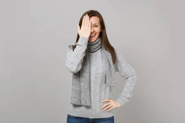 灰色のセーターで 若い女性の笑みを浮かべて 手で目を覆うスカーフはスタジオで灰色の壁の背景に分離 健康ファッション ライフ スタイル人誠実な感情寒い季節のコンセプト コピー スペースをモックアップします — ストック写真