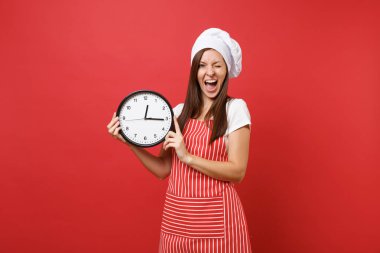 Ev hanımı kadın şef aşçı ya da baker izole kırmızı duvar arka plan üzerinde çizgili önlük, beyaz tişört, toque şefler şapkalı. Yuvarlak saat acele elinde tutan gülümseyen kadın. Kopyalama alanı kavramı alay