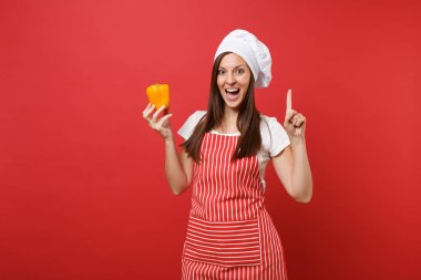 Ev hanımı kadın şef aşçı ya da baker Studio kırmızı duvar arka plan üzerinde izole çizgili önlük, beyaz tişört, toque şefler şapkalı. Gülümseyen kadın tutun el sarı biber. Kopyalama alanı kavramı alay