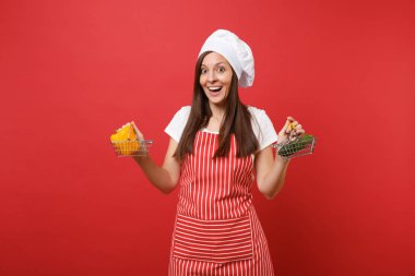 Ev hanımı kadın şef aşçı baker şapkalı izole kırmızı duvar arka plan üzerinde çizgili önlük beyaz t-shirt toque şefler. Kadın tutun sarı biber salatalık bakkal itme arabası sahte kopya alanı kavramı kadar