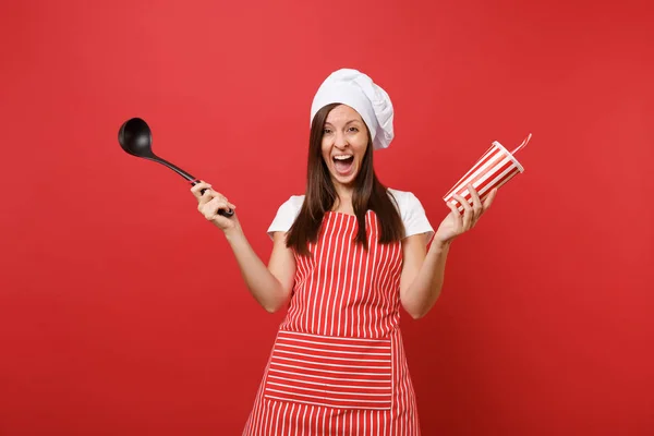 家庭主妇女厨师或面包师在条纹围裙 扭矩厨师帽查出的红色墙壁背景 女人拿着汤黑钢包铲 塑料杯可乐 模拟复制空间概念 — 图库照片