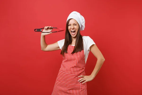 Female chef cook or baker in striped apron, white t-shirt toque chefs hat isolated on red wall background. Woman hold kitchen salad serving plastic pair of tongs for grill. Mock up copy space concept