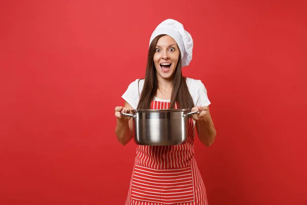 Housewife female chef cook or baker in striped apron white t-shirt toque chefs hat isolated on red wall background. Beautiful housekeeper woman holding vacant crockery pot. Mock up copy space concept